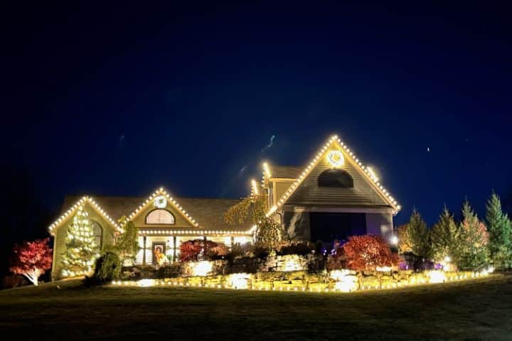 House illuminated with Christmas light installation. Festive holiday lights outline the roof and landscape, creating a warm glow against the night sky.